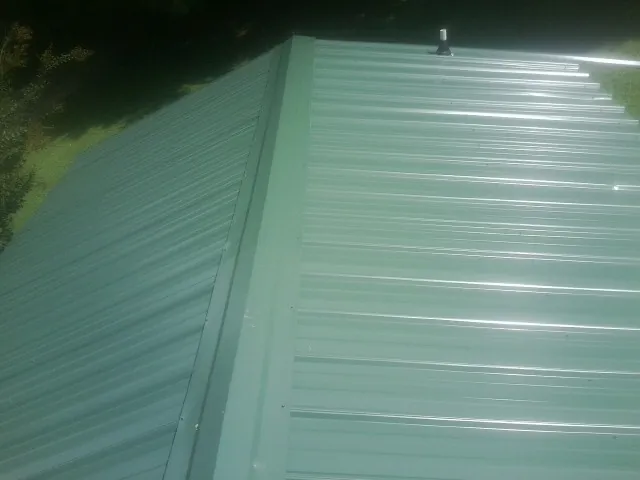 New green metal panels meeting at the ridge of a roof — Flat Roof Repair work by our crew in Barnesville